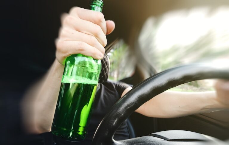 A person is holding a beer bottle and is about to get into a car accident.